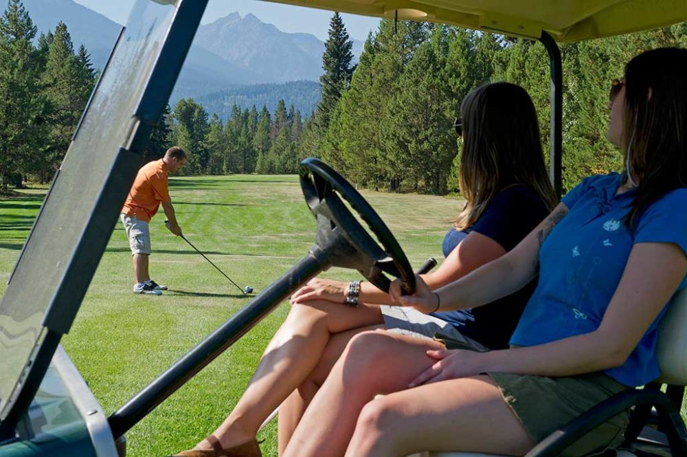 Women driving in golf cart, man teeing off